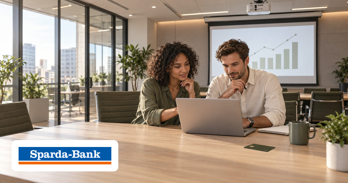 Ein Mann und eine Frau gemeinsam am Laptop im Büro, eine Kreditkarte auf dem Tisch und das Logo von Sparda-Bank unten links.