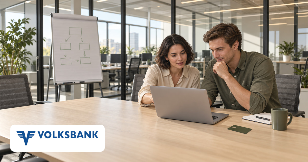Ein Mann und eine Frau gemeinsam am Laptop im Büro, eine Kreditkarte auf dem Tisch und das Logo von Volksbank Österreich unten links.